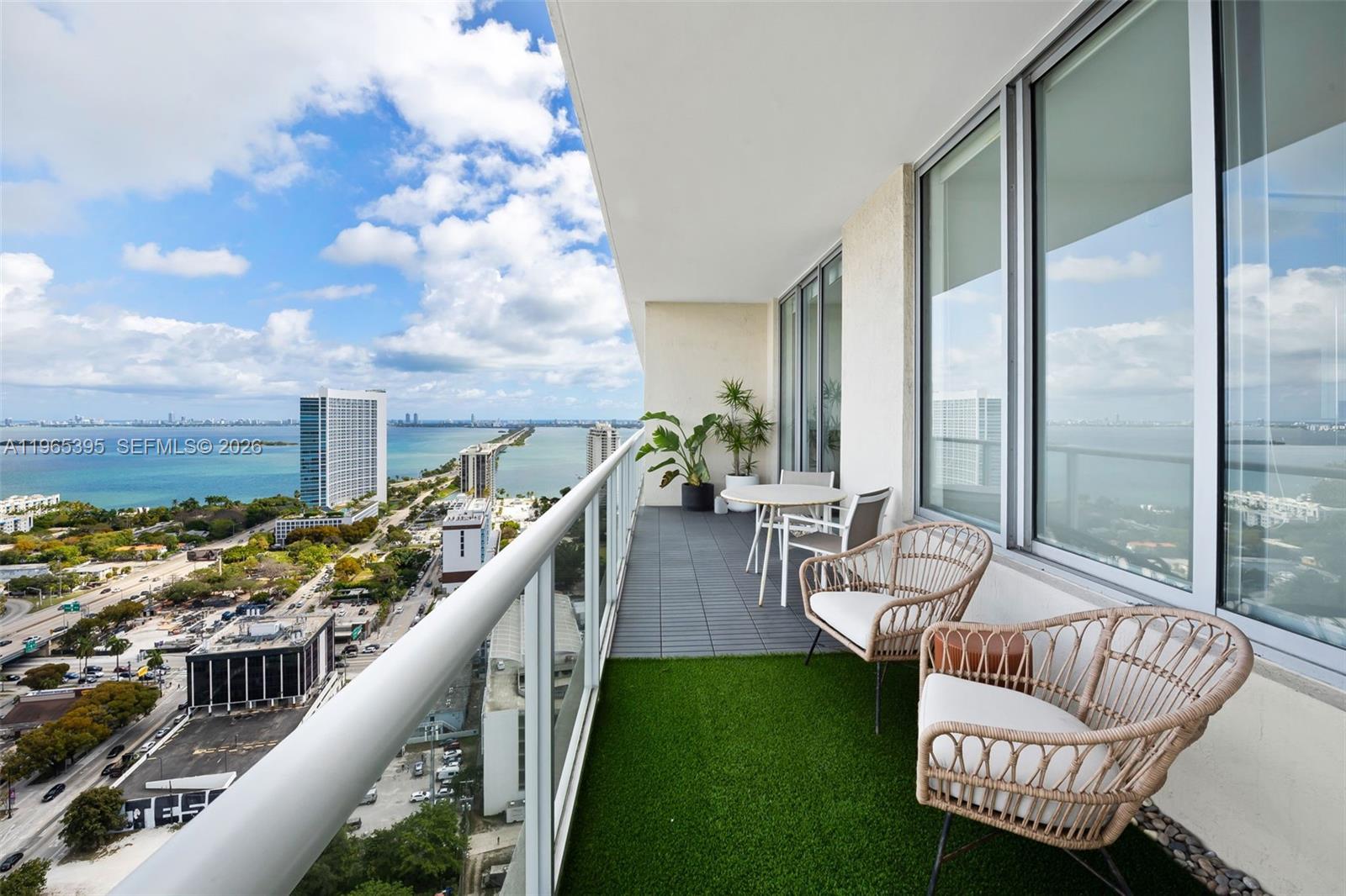 A balcony with artificial turf, wicker chairs, and a table overlooks a coastal city view — 3470 E Coast Ave, Miami FL 33137, MIAMI, FL
