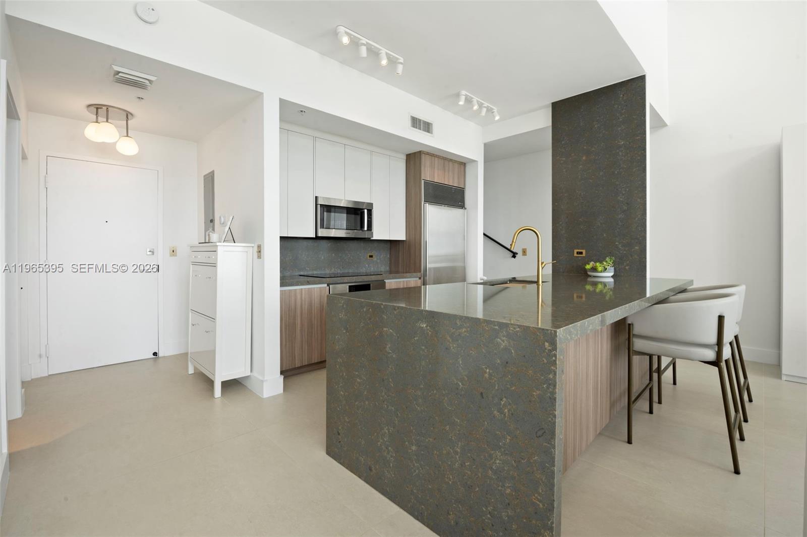 A modern kitchen features a stone-topped island, wood-toned cabinetry, and white upper cabinets — 3470 E Coast Ave, Miami FL 33137, MIAMI, FL
