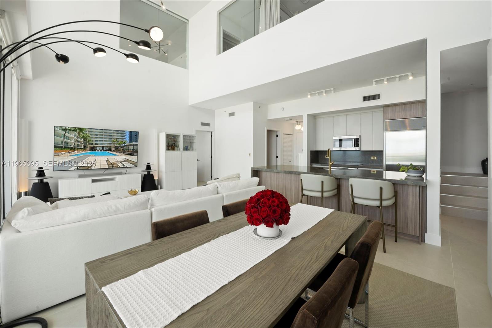 A modern, open-concept living and dining area features high ceilings, white furniture, and a kitchen — 3470 E Coast Ave, Miami FL 33137, MIAMI, FL