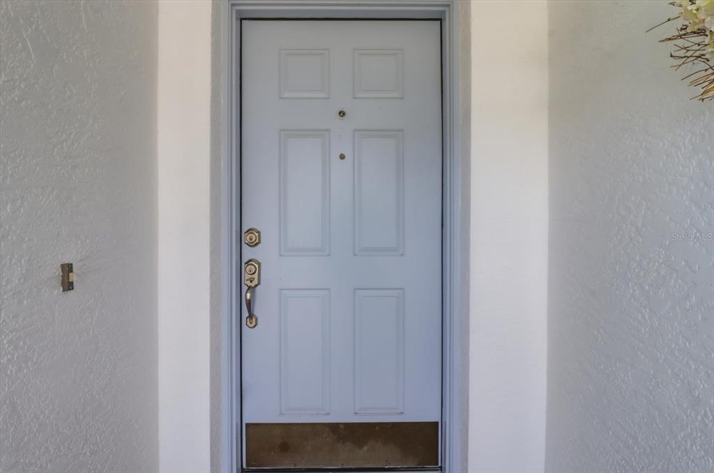 A white six-panel front door with a brass kickplate and hardware is set in a wall — 685 W COLBERT COURT, BEVERLY HILLS, FL