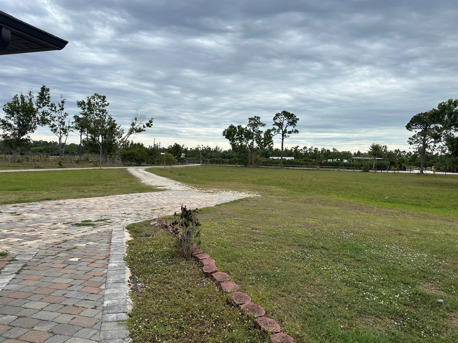 A paved driveway leads through a large grassy yard toward a line of trees — 3401 Sand Road, Cape Coral FL 33993, CAPE CORAL, FL