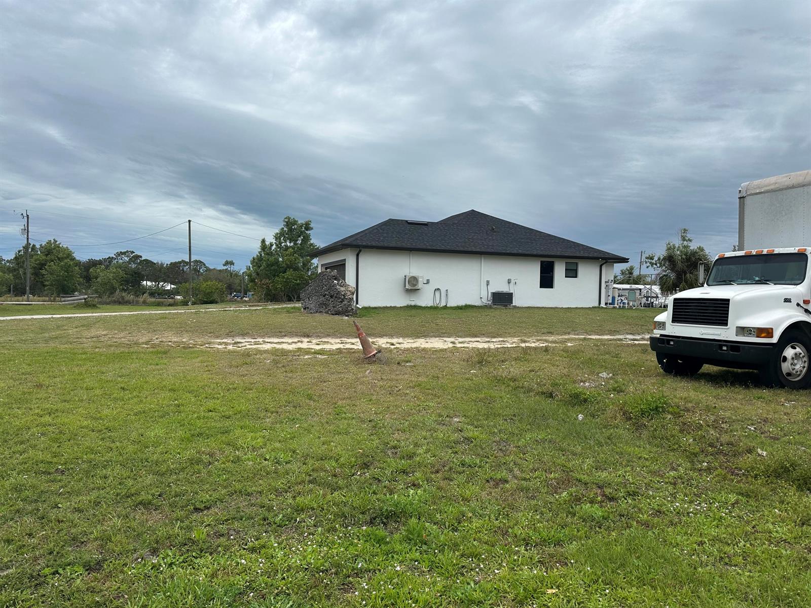 A white house with a dark roof sits on a large, grassy lot with a truck — 3401 Sand Road, Cape Coral FL 33993, CAPE CORAL, FL