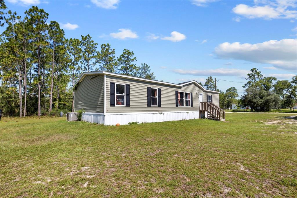 A single-story manufactured home with light green siding sits on a grassy lot — 390 NE 137TH AVENUE, WILLISTON, FL