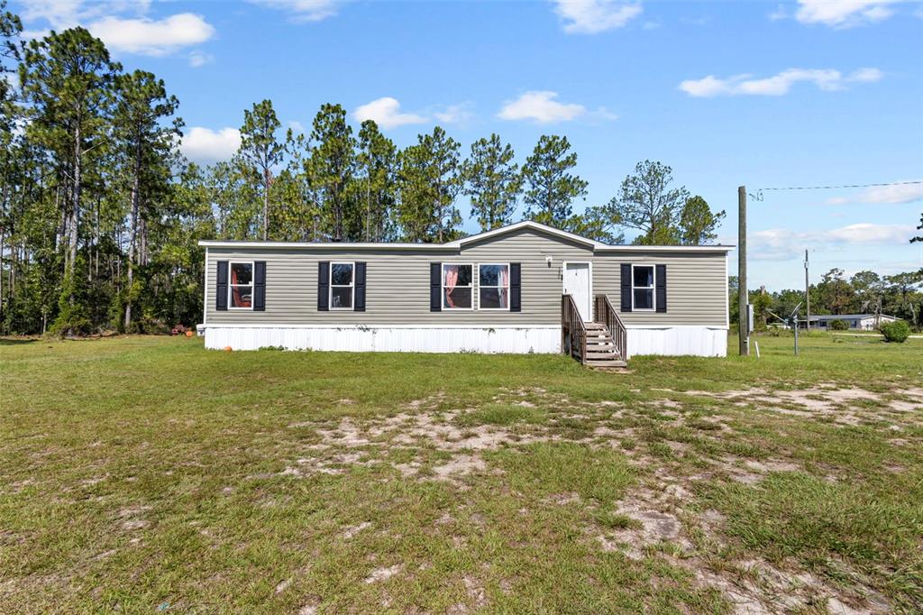 A single-story manufactured home with light gray siding sits on a large, grassy lot — 390 NE 137TH AVENUE, WILLISTON, FL