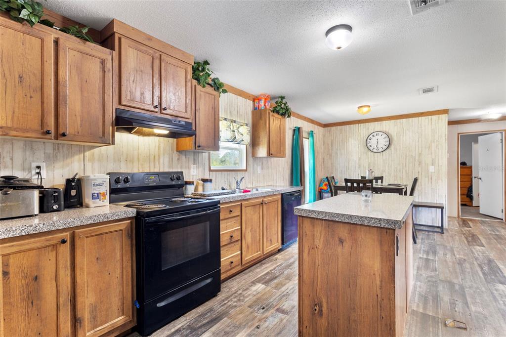 A kitchen with wood cabinets, black appliances, a center island, and wood-look flooring — 390 NE 137TH AVENUE, WILLISTON, FL