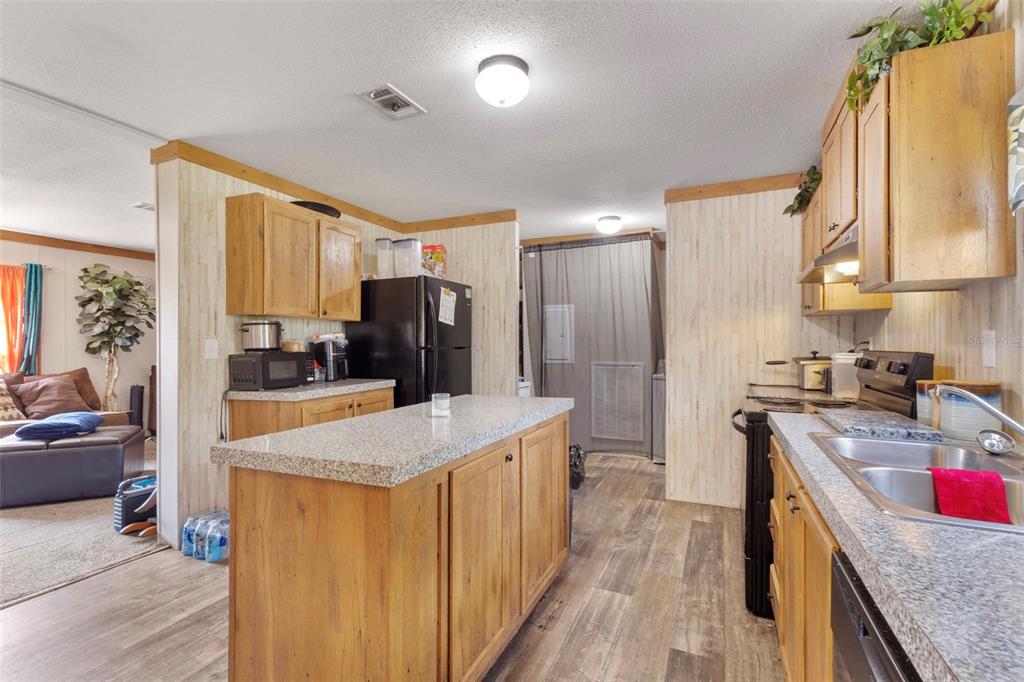 A kitchen features wood cabinets, a granite-topped island, and light-colored wood-look flooring — 390 NE 137TH AVENUE, WILLISTON, FL