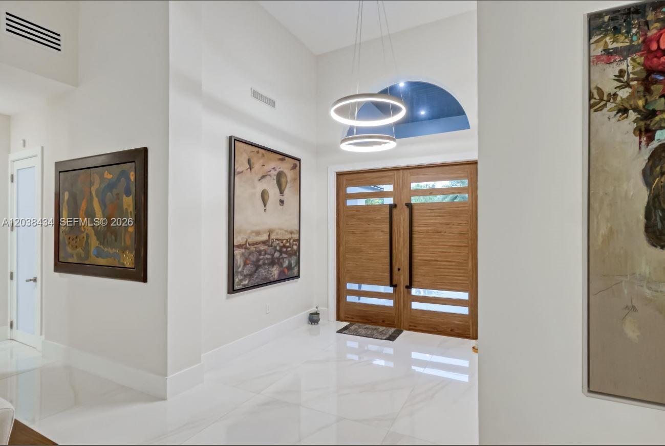 A bright entryway features white tile floors, double wooden doors, and modern circular pendant lighting — 11390 SW 30th St, Miami FL 33165, MIAMI, FL