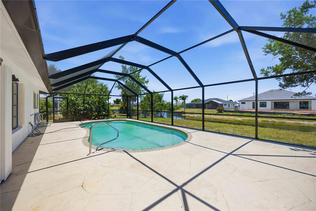 A screened-in pool patio overlooks a grassy yard and a small pond — 244 MARK TWAIN LANE, ROTONDA WEST, FL