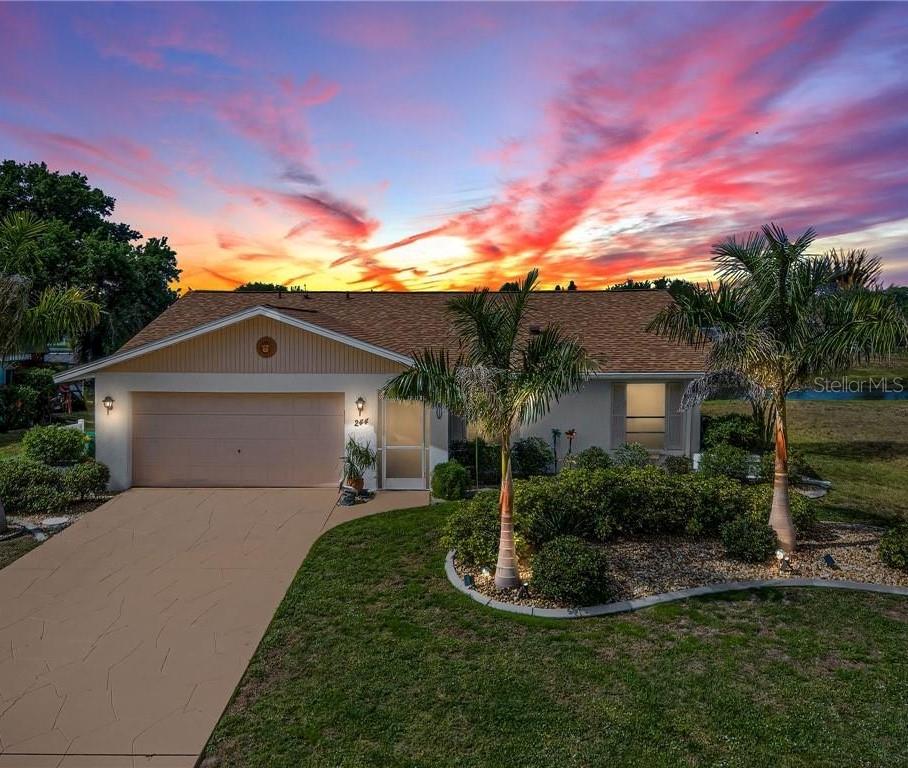 A single-story house with a two-car garage and palm trees under a vibrant sunset sky — 244 MARK TWAIN LANE, ROTONDA WEST, FL
