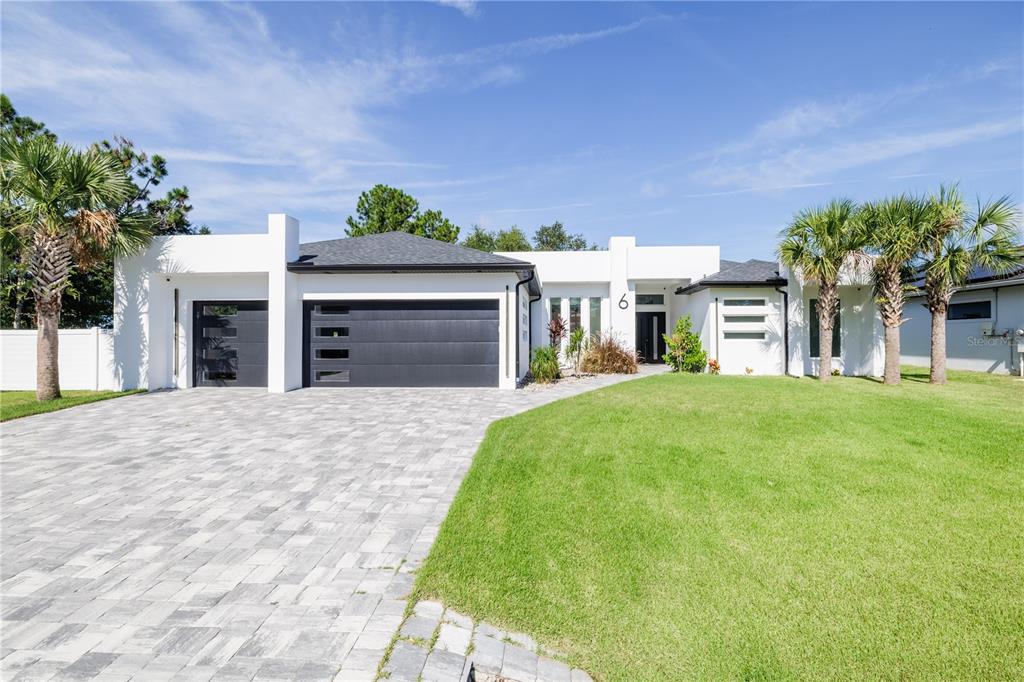 A modern single-story house with a paved driveway, dark garage doors, and white exterior walls — 6 ROCKNE LANE, PALM COAST, FL