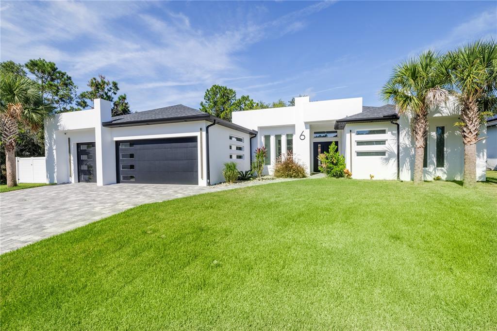 A modern white house with a black garage door and palm trees on a lawn — 6 ROCKNE LANE, PALM COAST, FL