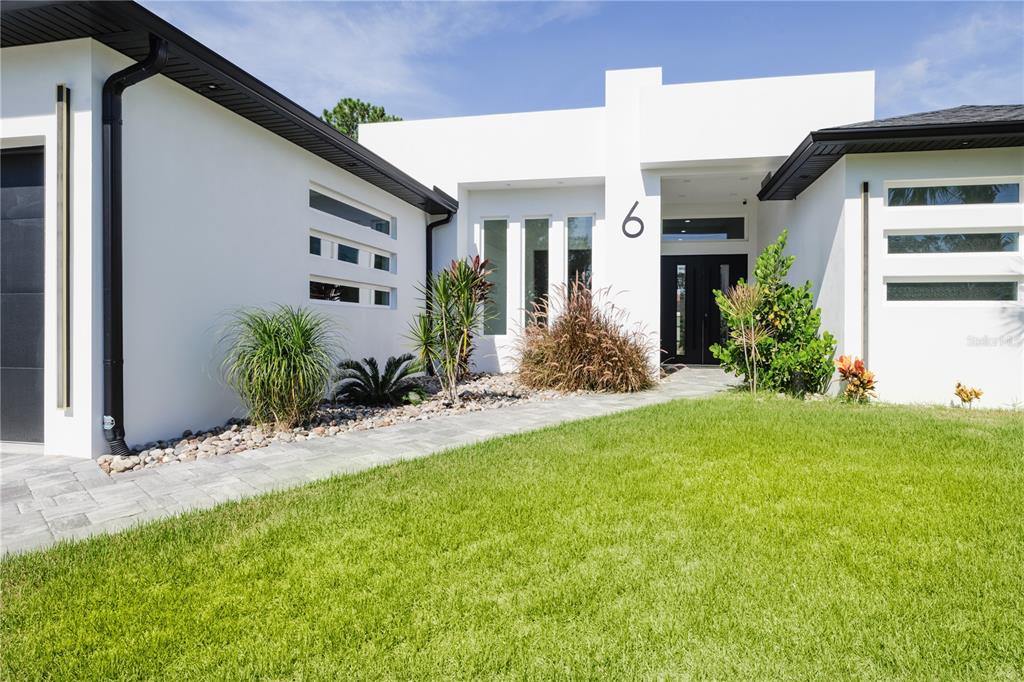 A modern white house with a flat roof, dark trim, and a paved walkway entrance — 6 ROCKNE LANE, PALM COAST, FL