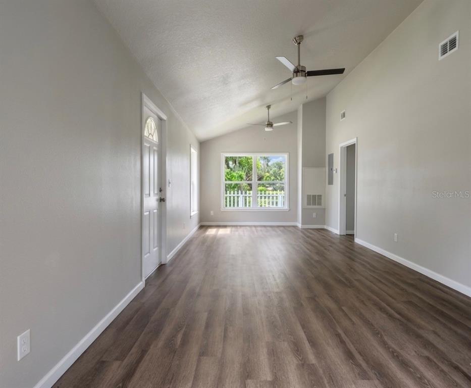 An empty room with light gray walls, wood-look flooring, vaulted ceilings, and two ceiling fans — 343 N MAIN AVENUE, GROVELAND, FL