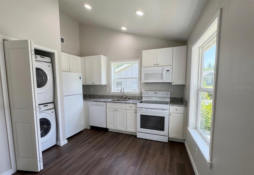 A kitchen features white cabinets, white appliances, granite countertops, and a stacked washer and dryer — 343 N MAIN AVENUE, GROVELAND, FL