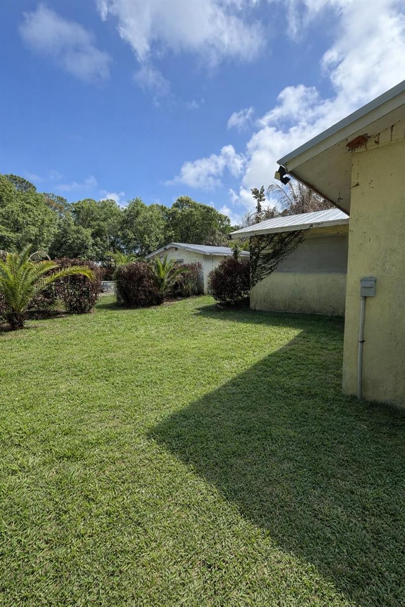 A grassy backyard features a yellow house exterior, a detached structure, and various shrubs — 5512 Buchanan Drive, Fort Pierce FL 34982, FORT PIERCE, FL