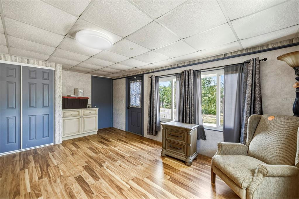 A room with wood-look flooring, a drop ceiling, blue doors, and a beige armchair — 5590 W MCDOWELL LANE, DUNNELLON, FL