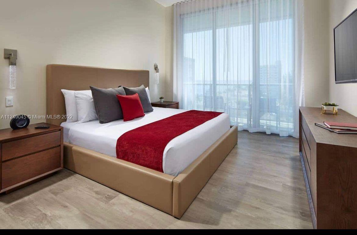 A bedroom features a platform bed with a red runner, wood furniture, and a balcony view — 777 N Ocean Dr # N323, Hollywood FL 33019, HOLLYWOOD, FL