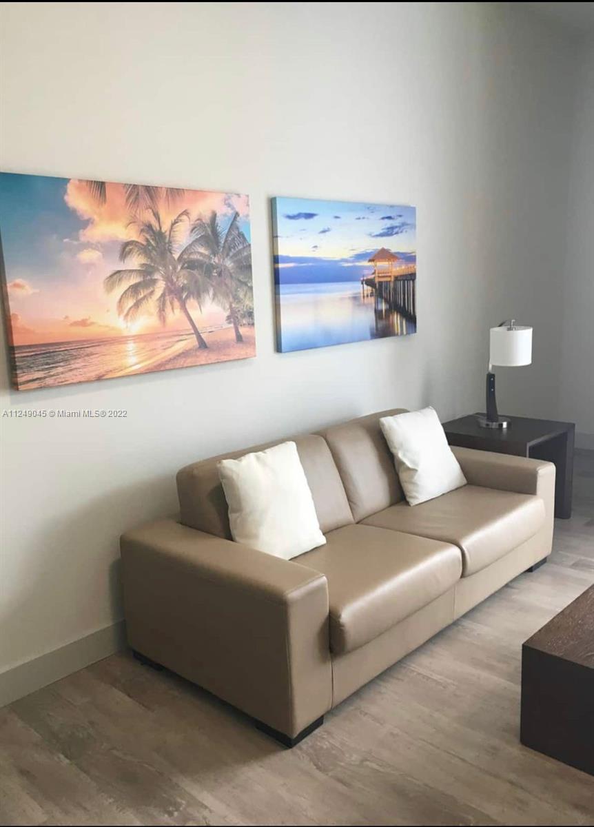 A living room features a tan leather sofa, two wall art prints, and a side lamp — 777 N Ocean Dr # N323, Hollywood FL 33019, HOLLYWOOD, FL