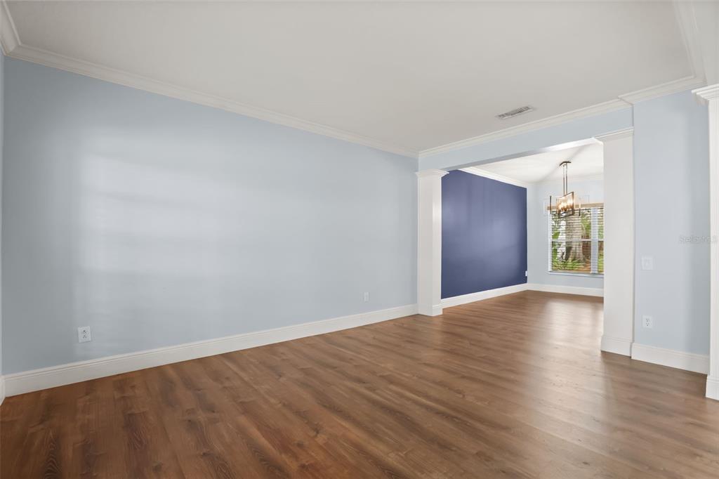 An empty room with light blue walls, wood-look flooring, and an opening to a dining area — 1800 PINE BAY DRIVE, LAKE MARY, FL