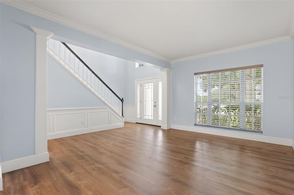 An empty room with light blue walls, wood-look flooring, a staircase, and a front door — 1800 PINE BAY DRIVE, LAKE MARY, FL