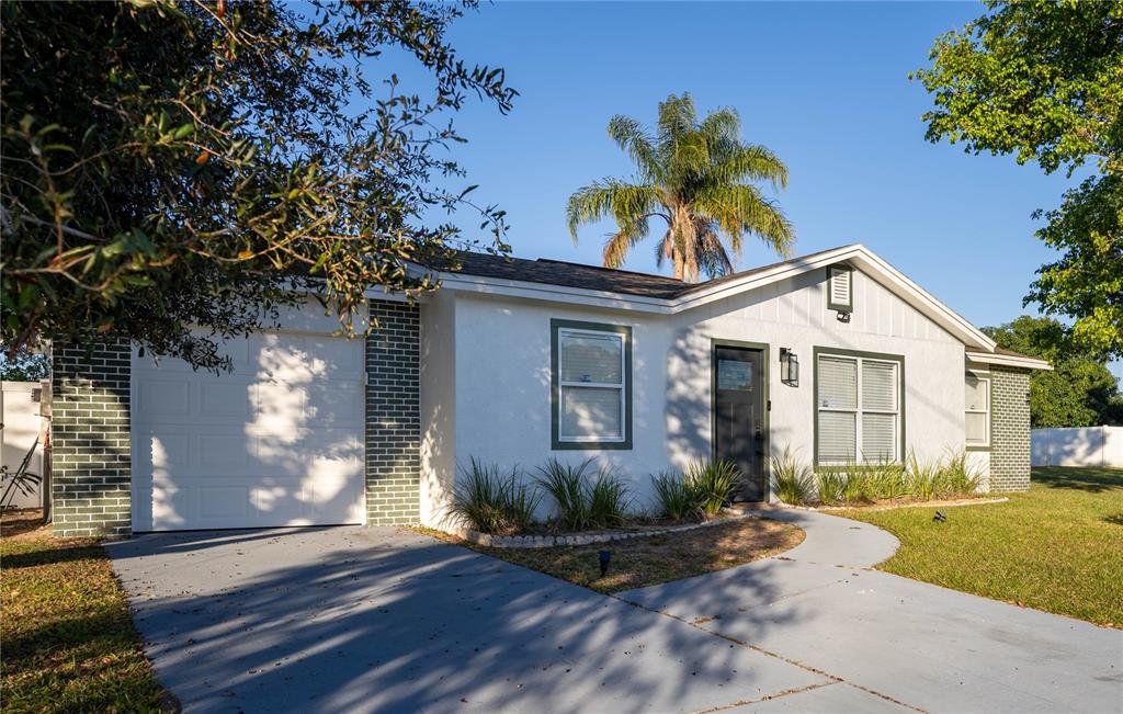A single-story house with a white stucco facade, green brick accents, and a gray driveway — 315 LAUDERDALE COURT, KISSIMMEE, FL