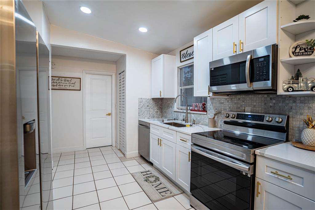 A kitchen features white cabinets, stainless steel appliances, a tiled backsplash, and white floor tiles — 315 LAUDERDALE COURT, KISSIMMEE, FL