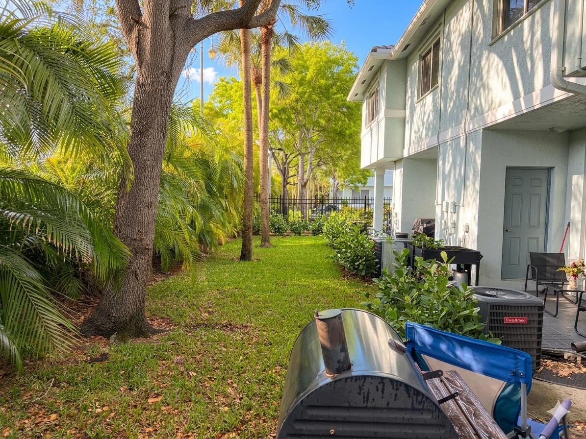 A grassy backyard area features a large tree, palm trees, and a two-story house exterior — 3731 Sonoma Drive, Riviera Beach FL 33404, RIVIERA BEACH, FL
