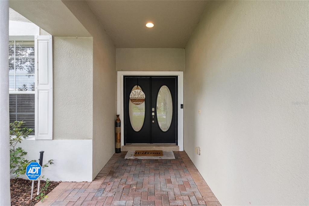A covered entryway features a brick-paved porch leading to black double doors with oval glass — 15319 MONTAUK LANE, CLERMONT, FL