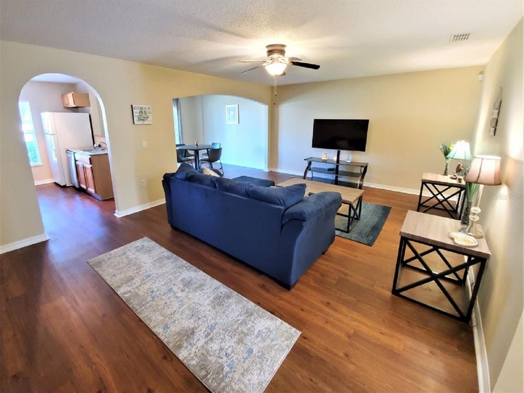A living room with wood-look flooring, a blue sofa, and an arched entryway to the kitchen — 9870 ASHBURN LAKE DRIVE, TAMPA, FL
