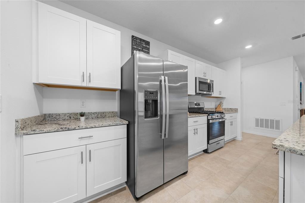 A kitchen features white cabinets, granite countertops, and stainless steel appliances — 7396 CAPSTONE DRIVE, GROVELAND, FL