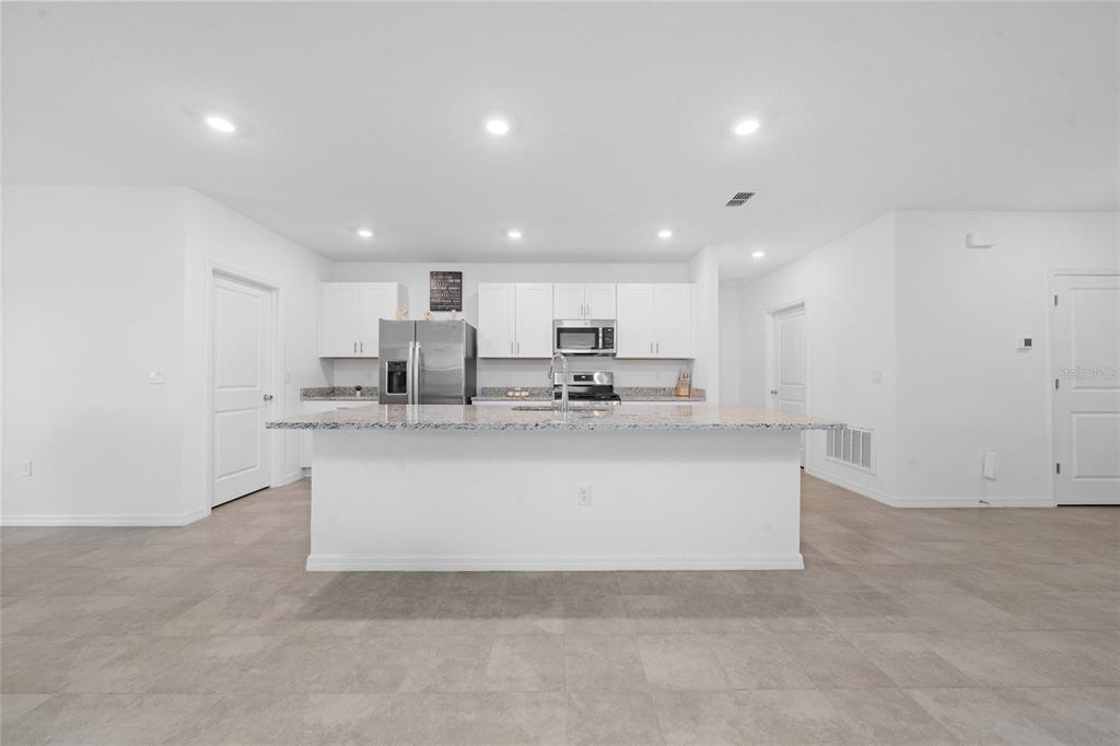 A modern kitchen features white cabinetry, granite countertops, a central island, and light tile flooring — 7396 CAPSTONE DRIVE, GROVELAND, FL