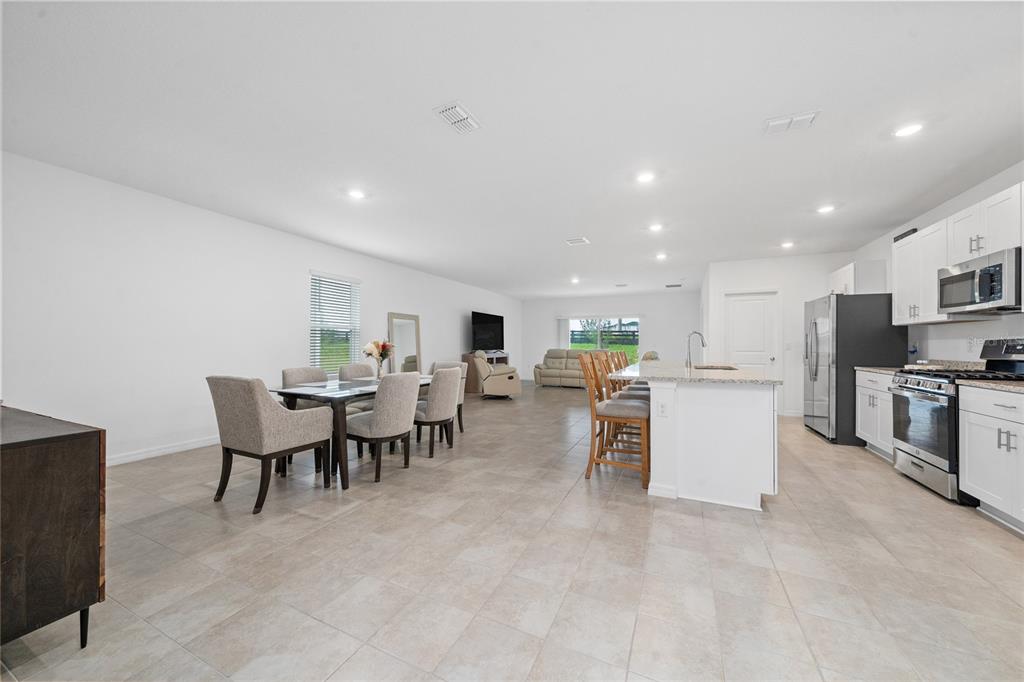 An open-concept kitchen, dining area, and living room with tile flooring and white cabinetry — 7396 CAPSTONE DRIVE, GROVELAND, FL