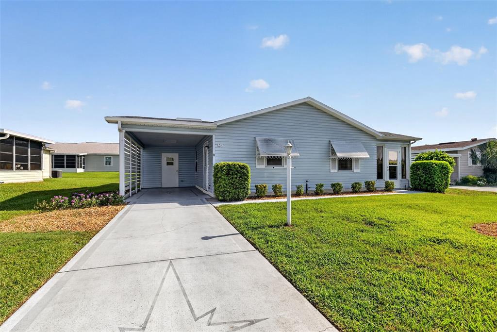 A light blue single-story house features a concrete driveway, a carport, and a grassy lawn — 1231 ZAPATA PLACE, LADY LAKE, FL