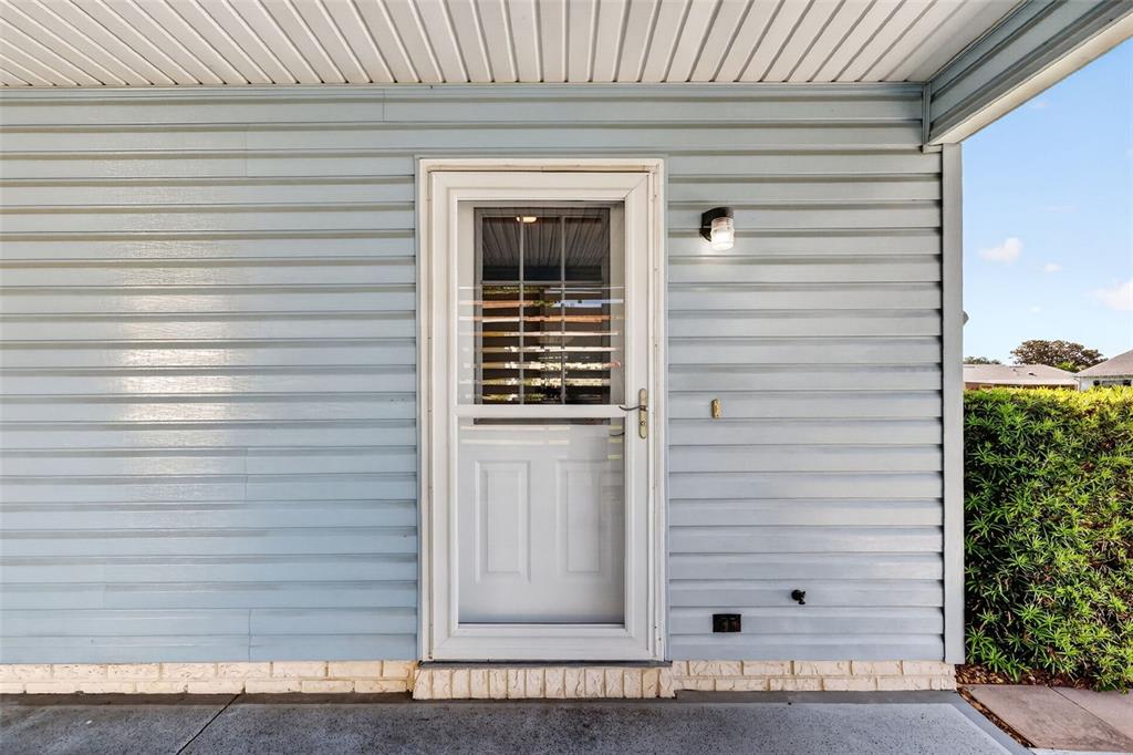 A white storm door is centered on a light blue vinyl-sided exterior wall — 1231 ZAPATA PLACE, LADY LAKE, FL