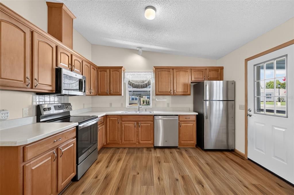 A kitchen features wood cabinets, stainless steel appliances, white countertops, and wood-look flooring — 1231 ZAPATA PLACE, LADY LAKE, FL
