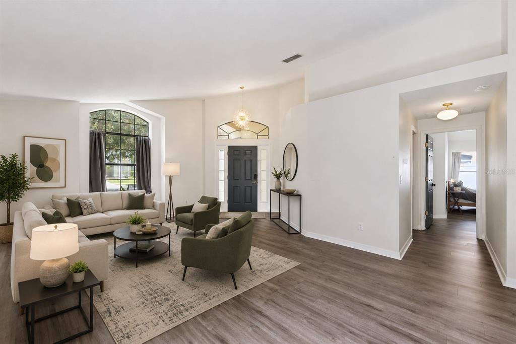 A bright living room features high ceilings, wood-look flooring, a dark front door, and furniture — 6629 WINDER OAKS BOULEVARD, ORLANDO, FL