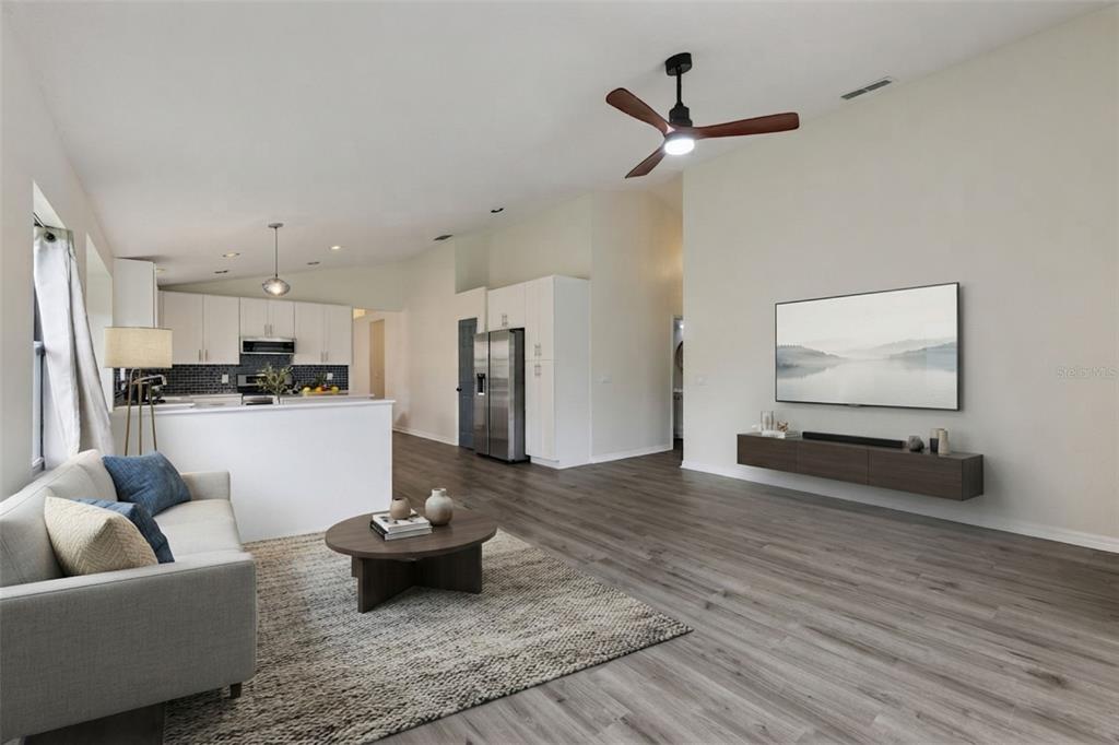 A living room with wood-look flooring, a ceiling fan, and an open kitchen in back — 6629 WINDER OAKS BOULEVARD, ORLANDO, FL