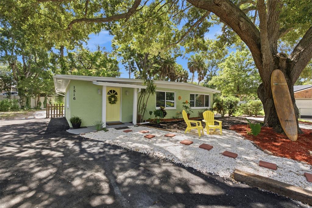 A light green single-story house features a yellow front door, white gravel path, and surfboard — 1516 ADELE PLACE, LARGO, FL