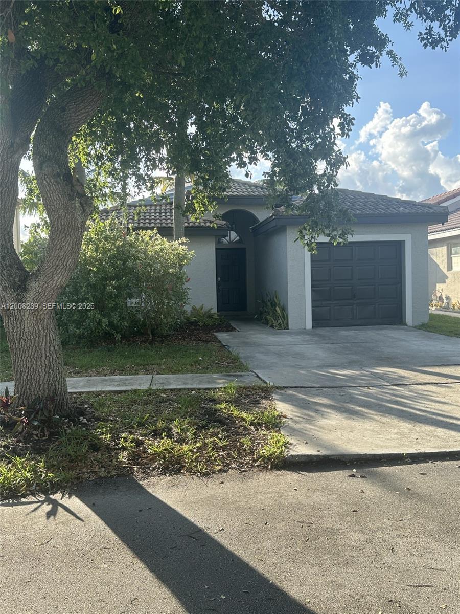 A single-story house with a dark garage door, a front entrance, and a large tree — 18022 SW 29th Ln, Miramar FL 33029, MIRAMAR, FL