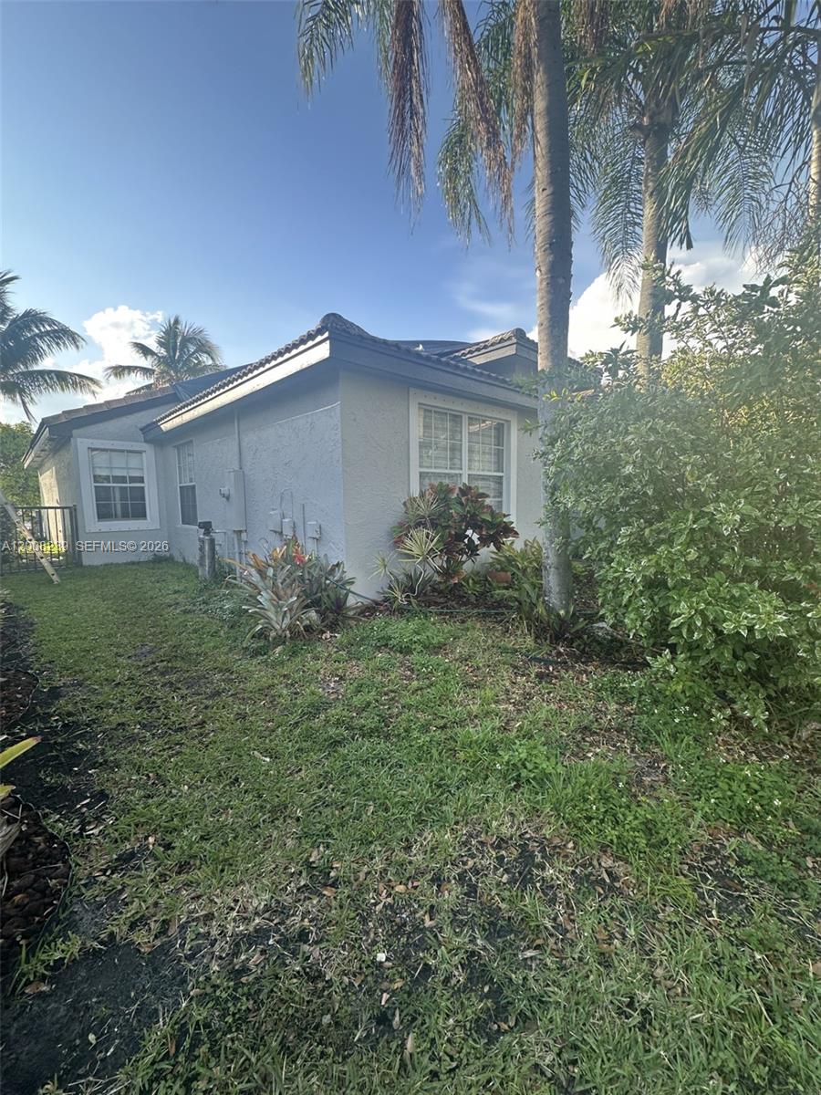 The exterior of a light-colored, single-story house features a lawn, palm trees, and landscaping — 18022 SW 29th Ln, Miramar FL 33029, MIRAMAR, FL