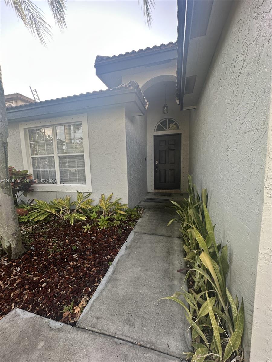 A concrete walkway leads to the dark front door of a stucco house — 18022 SW 29th Ln, Miramar FL 33029, MIRAMAR, FL
