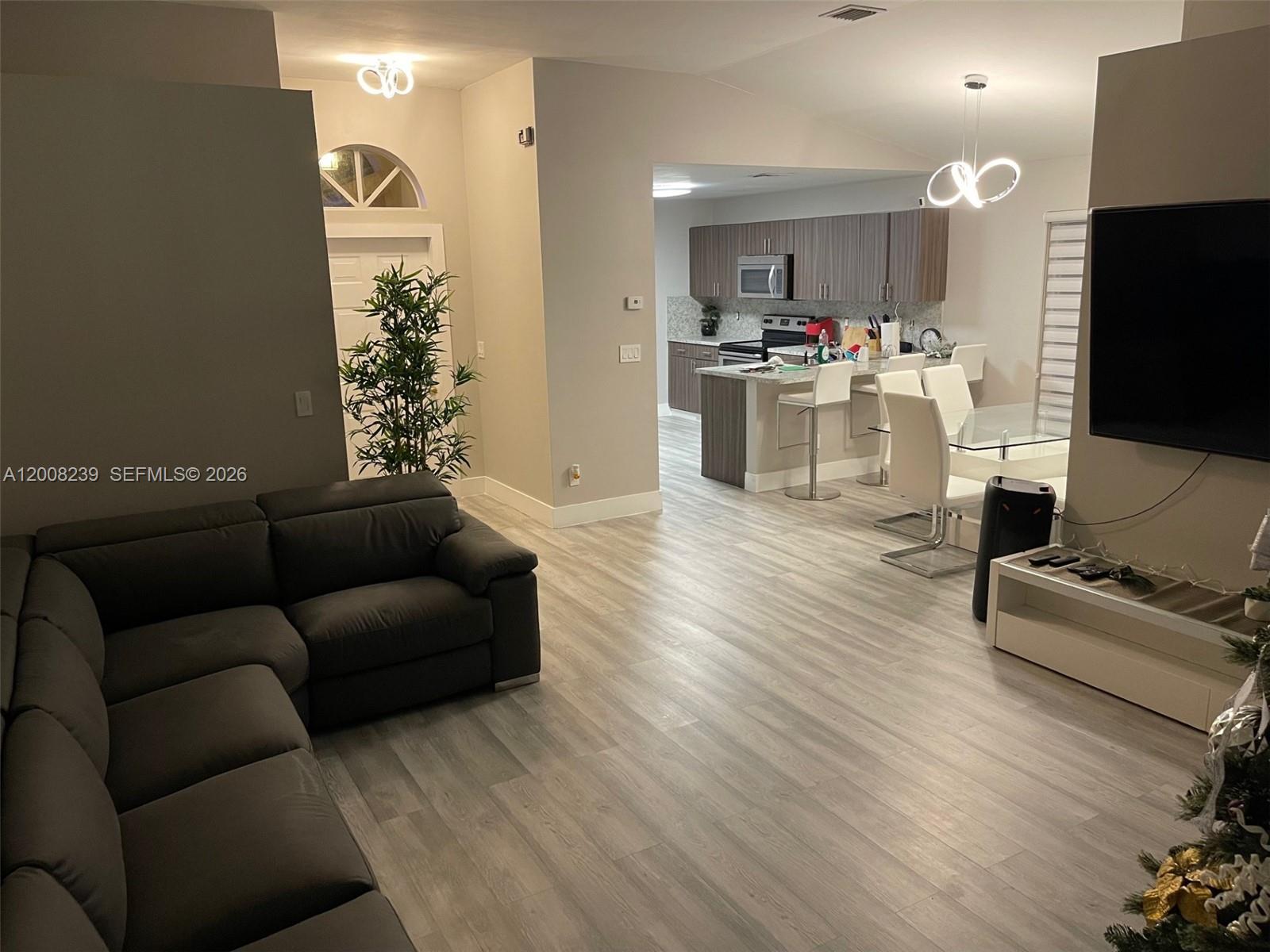 An open-concept living room and kitchen feature gray wood-look flooring and modern light fixtures — 18022 SW 29th Ln, Miramar FL 33029, MIRAMAR, FL