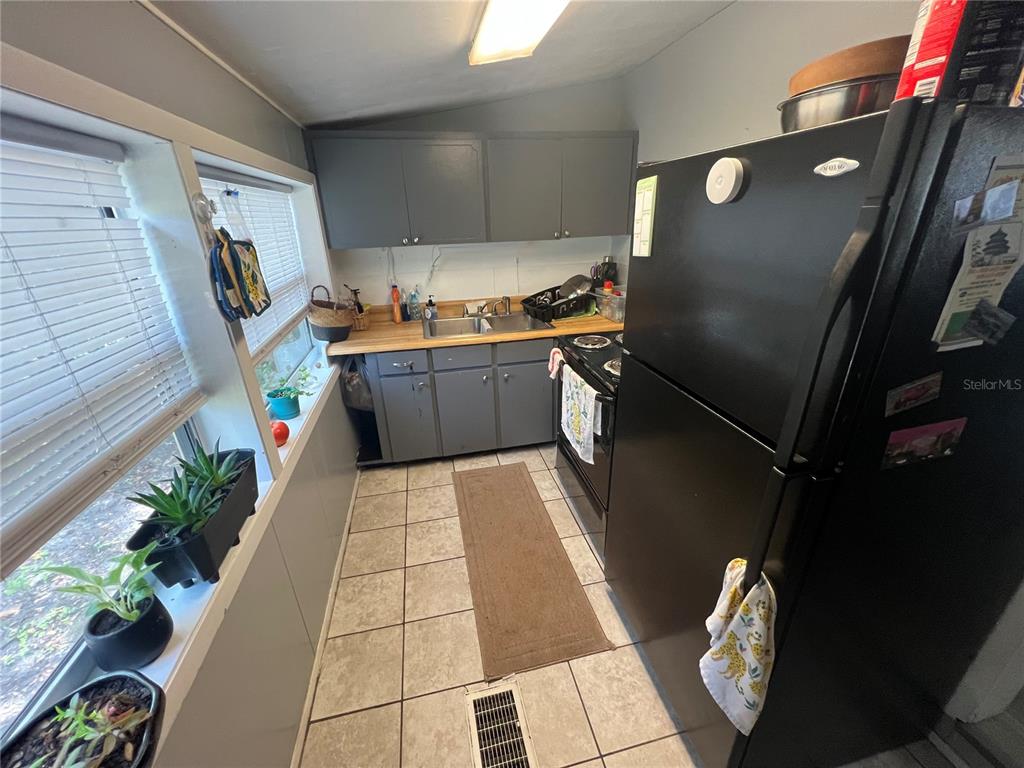 A narrow kitchen features gray cabinets, a wood countertop, black appliances, and tiled flooring — 6724 COUNTY ROAD 214, KEYSTONE HEIGHTS, FL