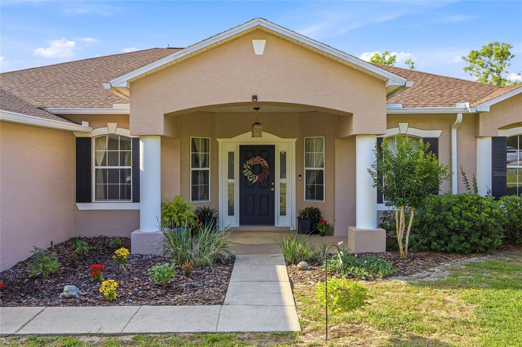 A tan house exterior features a covered entryway with white columns and a dark door — 11578 SW 50TH CIRCLE, OCALA, FL