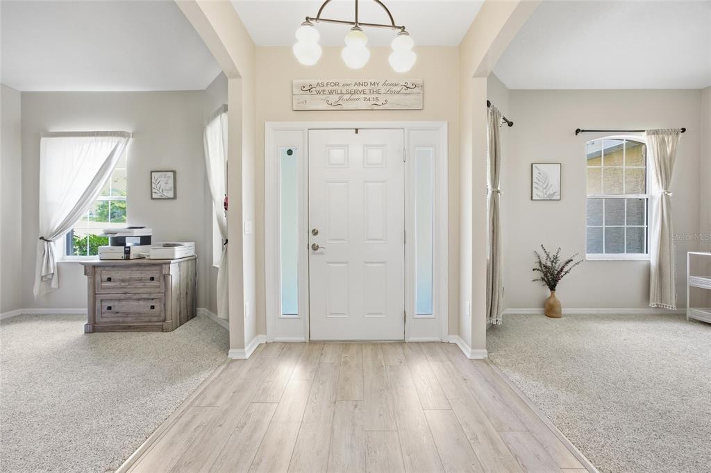 A bright entryway features light wood-look flooring, a white front door, and beige carpeted rooms — 11578 SW 50TH CIRCLE, OCALA, FL