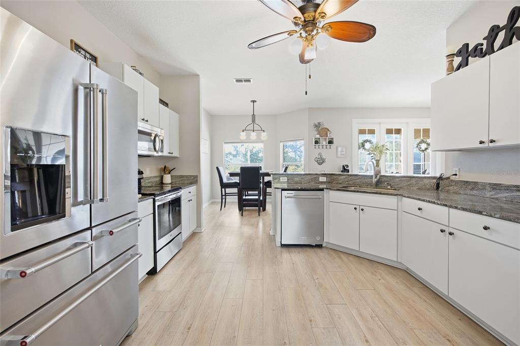 A kitchen with white cabinets, stainless steel appliances, and granite countertops opens to a dining area — 11578 SW 50TH CIRCLE, OCALA, FL