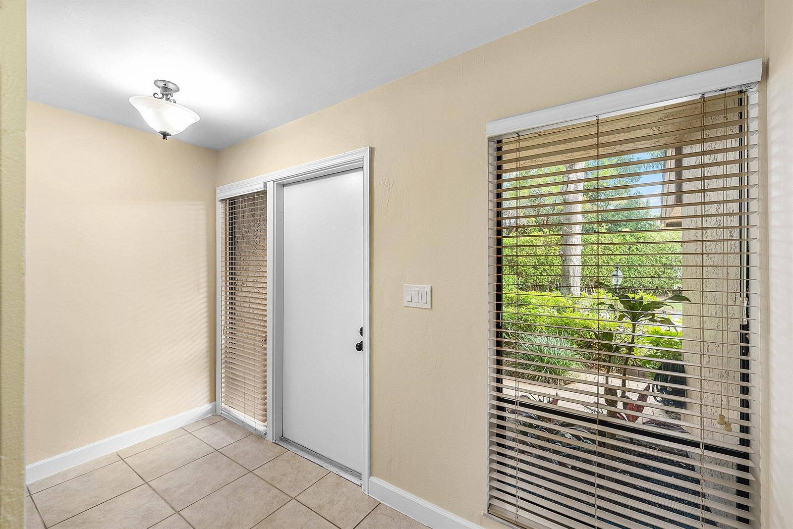 An entryway with beige walls, tile flooring, a white door, and large windows with blinds — 5664 Santiago Circle, Boca Raton FL 33433, BOCA RATON, FL