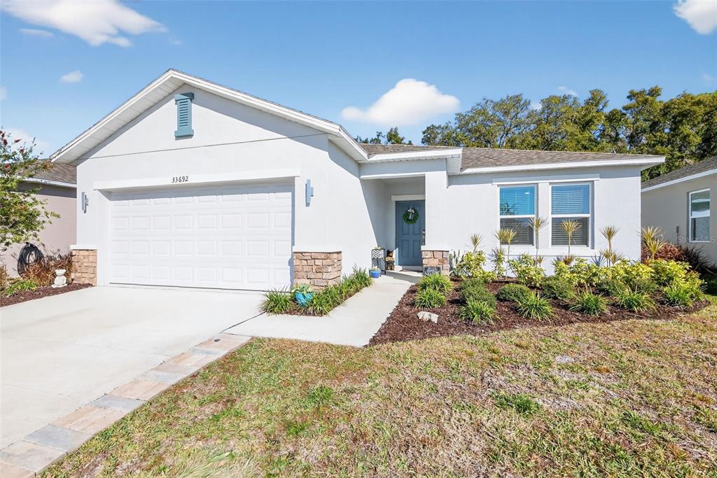 A single-story house with a white stucco exterior, stone accents, and a two-car garage — 33692 SKY BLOSSOM CIRCLE, LEESBURG, FL