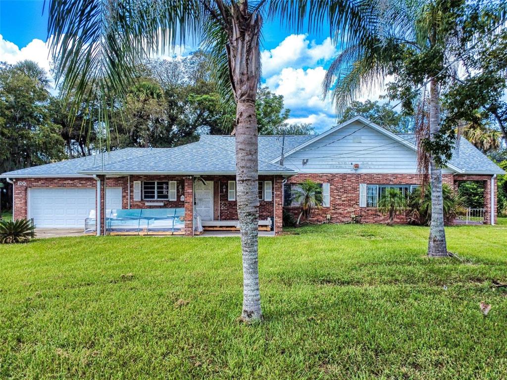 A single-story brick house with a white garage, a front porch, and two palm trees — 120 RAILROAD AVENUE, OSTEEN, FL