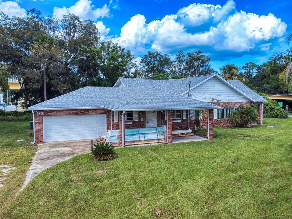 A single-story brick house with a gray shingled roof, a garage, and a covered porch — 120 RAILROAD AVENUE, OSTEEN, FL